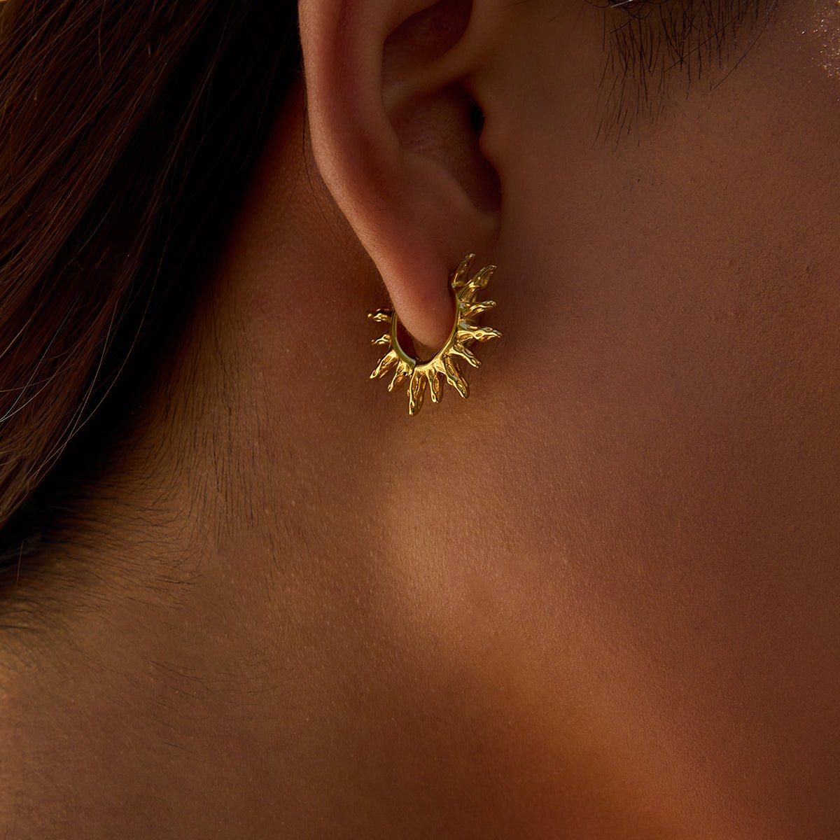 Gold earring worn on an ear with a blurred background