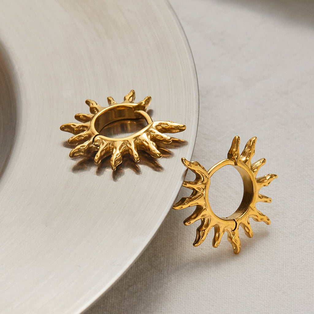 Gold sun-shaped earrings on a light background