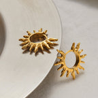 Gold sun-shaped earrings on a light background