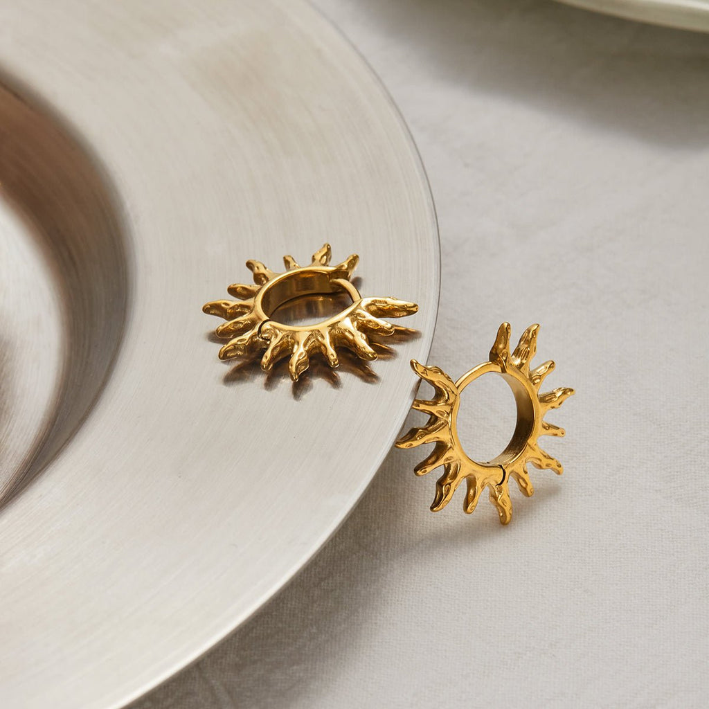 Gold sun-shaped earrings on a light surface