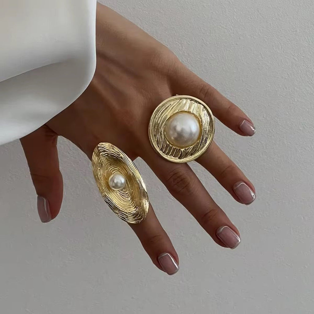 Gold earrings with pearl centers on a hand against a neutral background