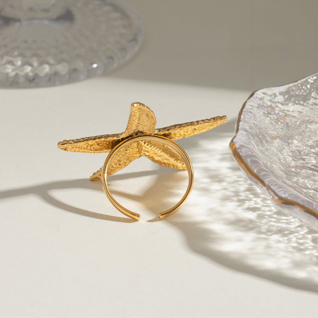 Gold starfish-shaped ring on a light surface with a textured background