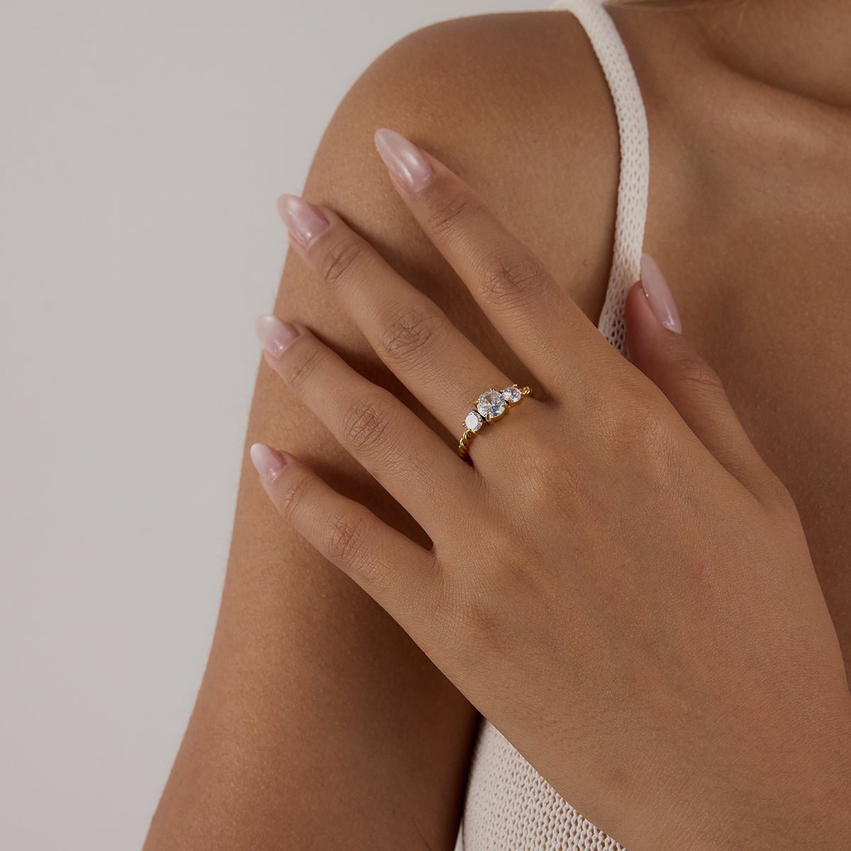 Close-up of a hand wearing a gold ring with a diamond on a neutral background