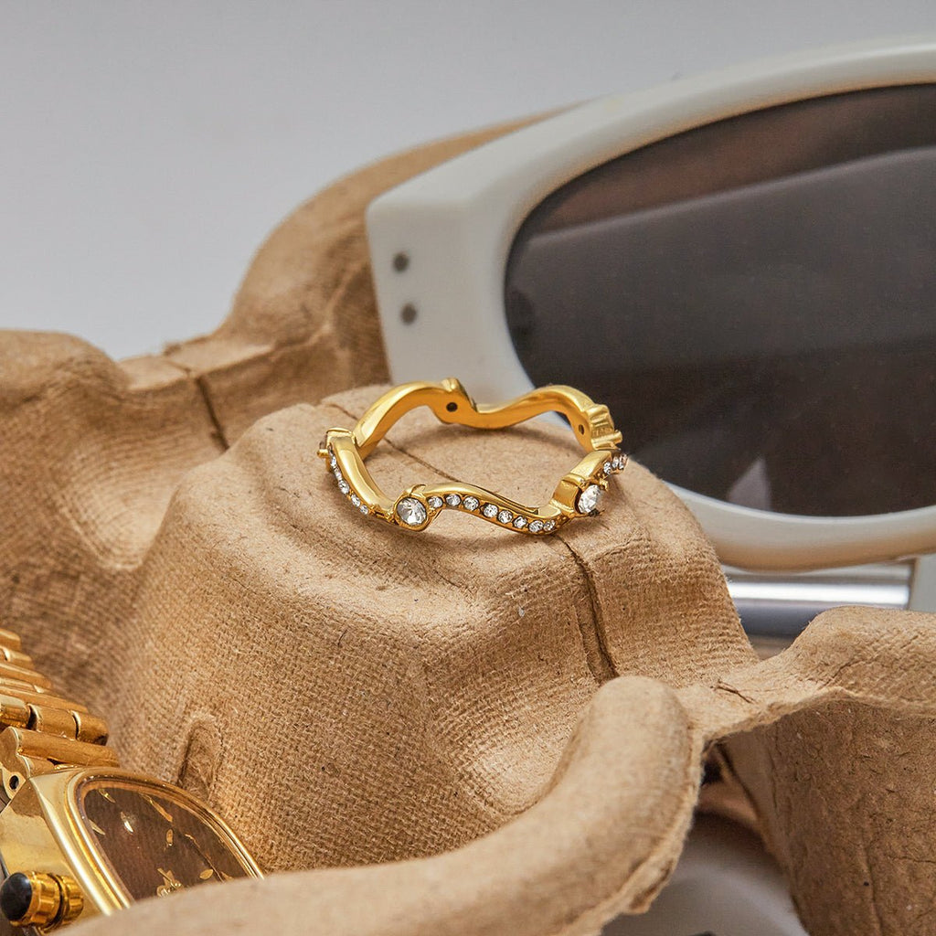 Gold ring with heart design on a textured surface with sunglasses in the background