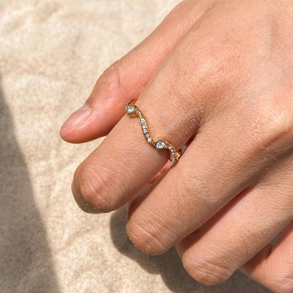 Close-up of a hand wearing a gold ring with gemstones on a beige background