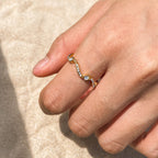 Close-up of a hand wearing a gold ring with gemstones on a beige background