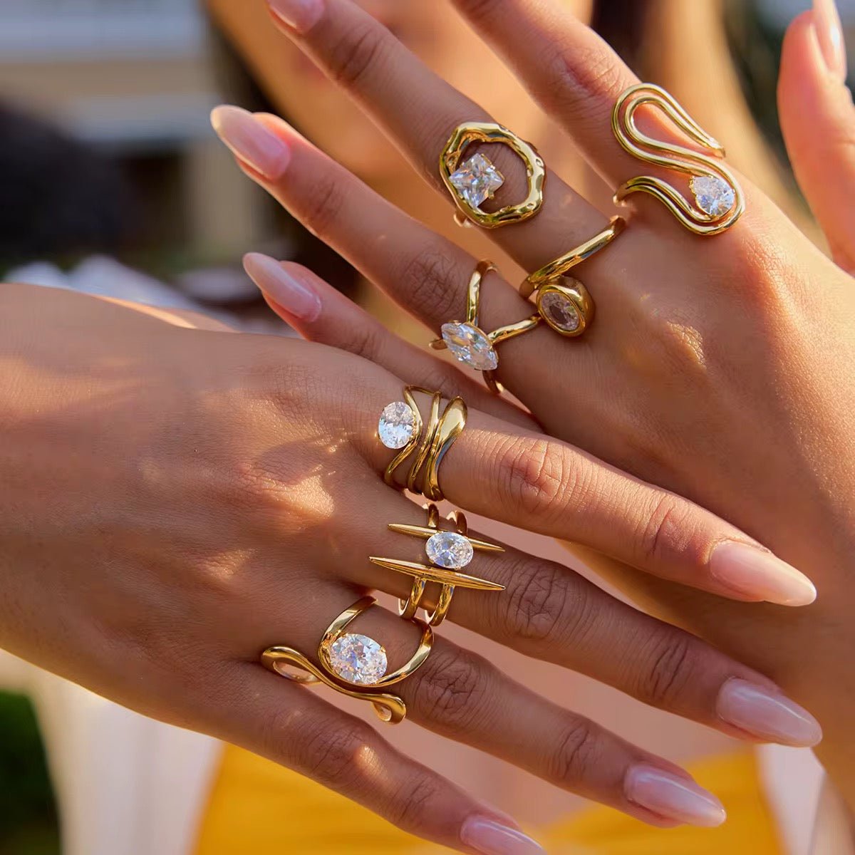 Close-up of hands wearing gold rings with gemstones on a blurred background