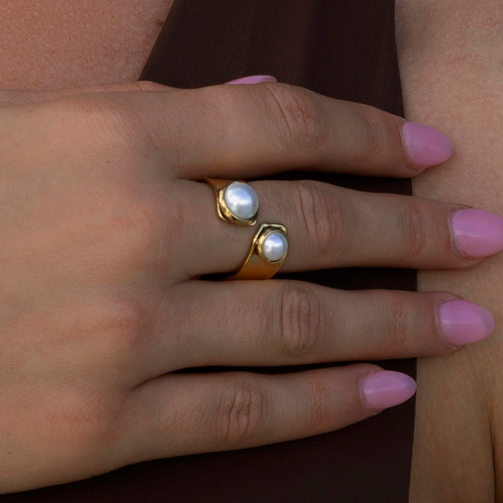 Close-up of a hand wearing two pearl rings on a plain background