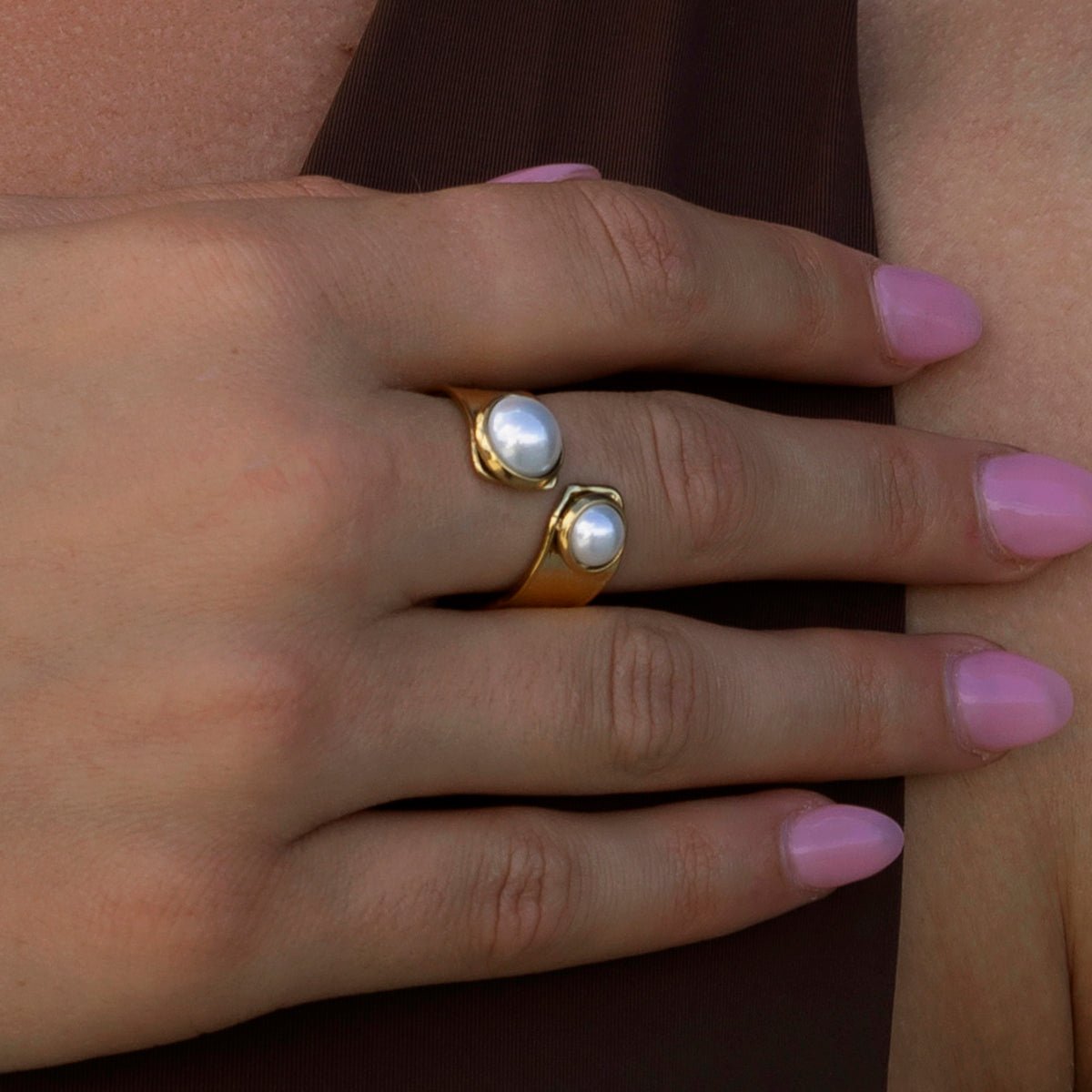Close-up of a hand wearing two pearl rings on a plain background