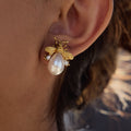 Gold bee-shaped earring with a pearl on an ear