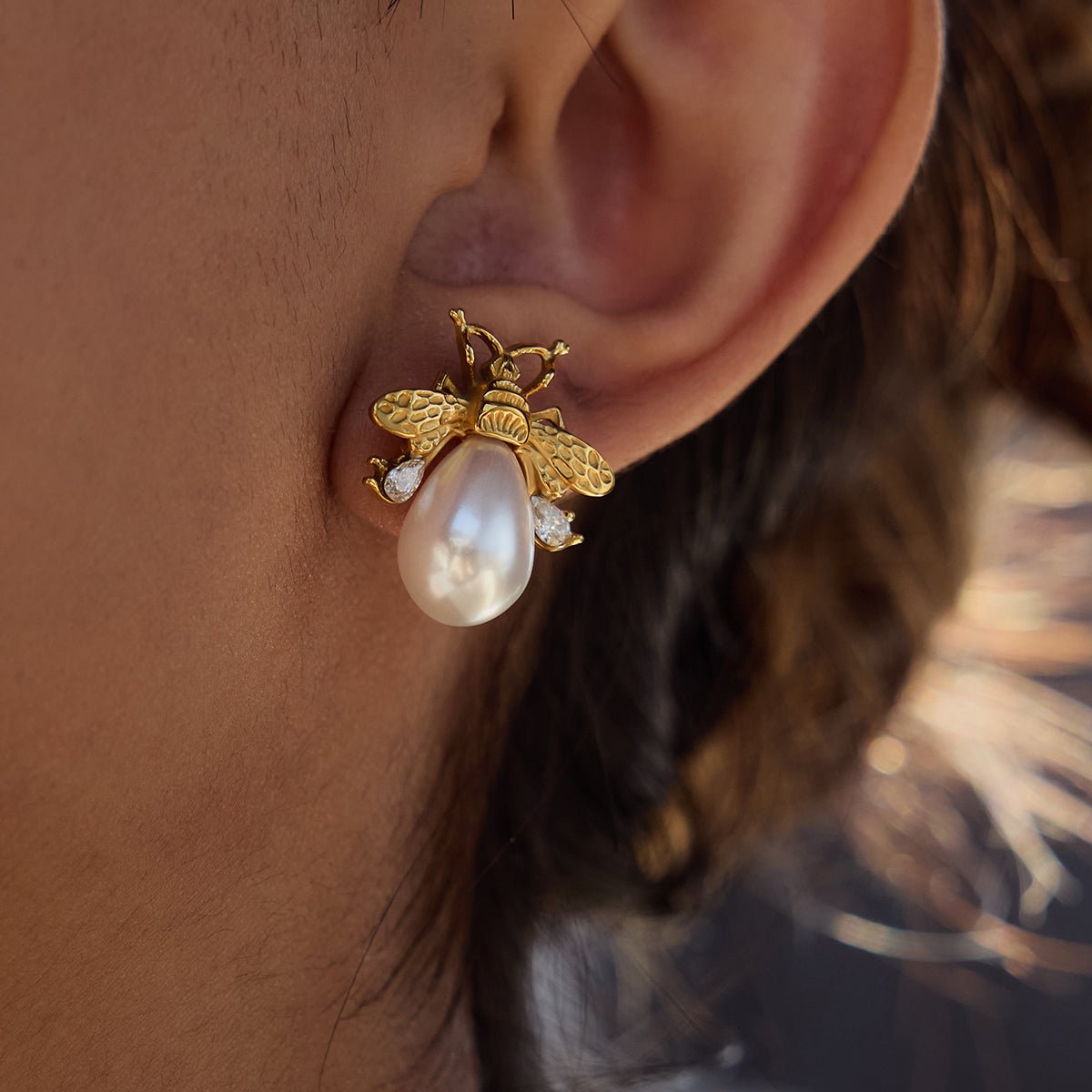 Gold bee-shaped earring with a pearl on an ear