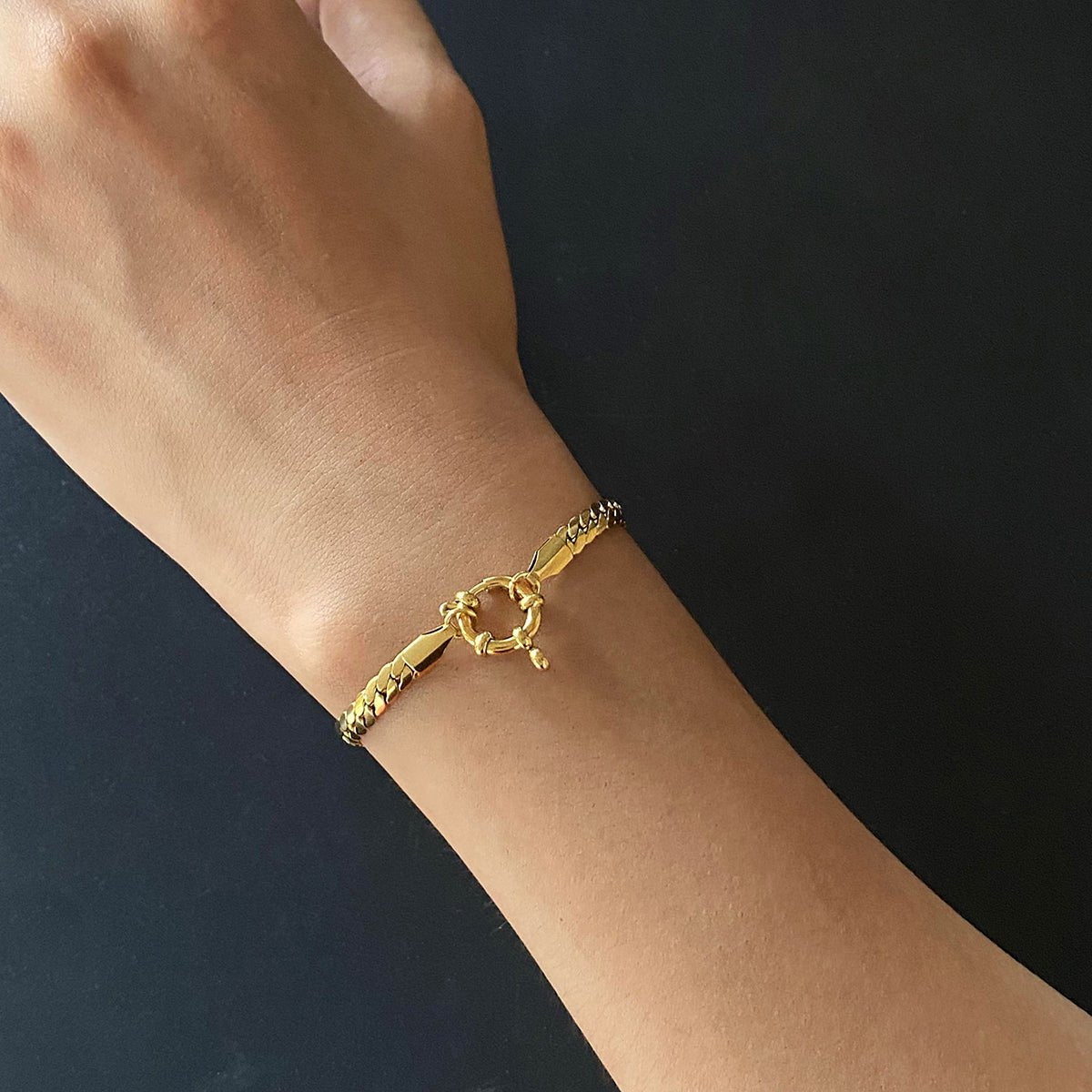 Gold bracelet on a wrist against a dark background