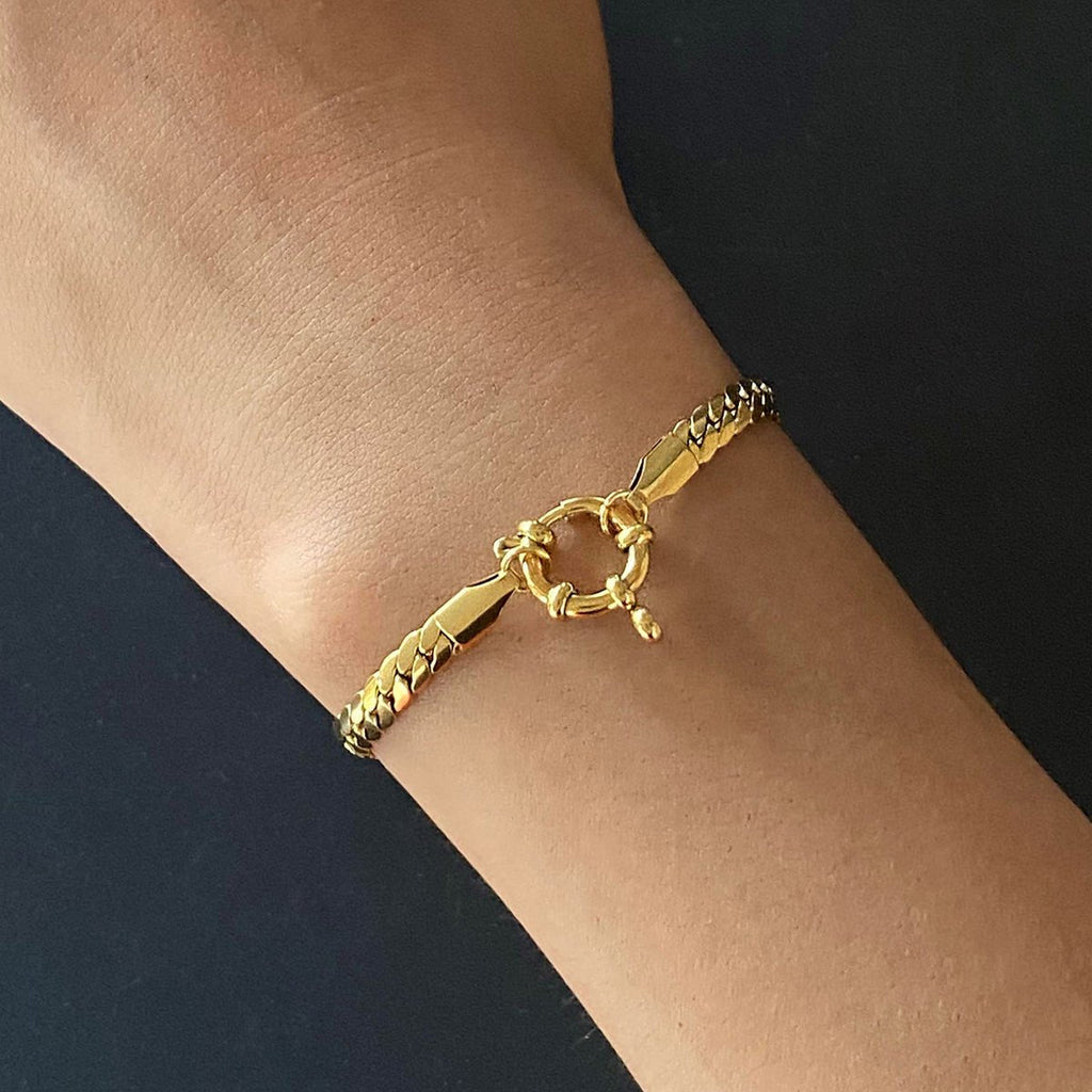 Gold bracelet on a wrist against a dark background