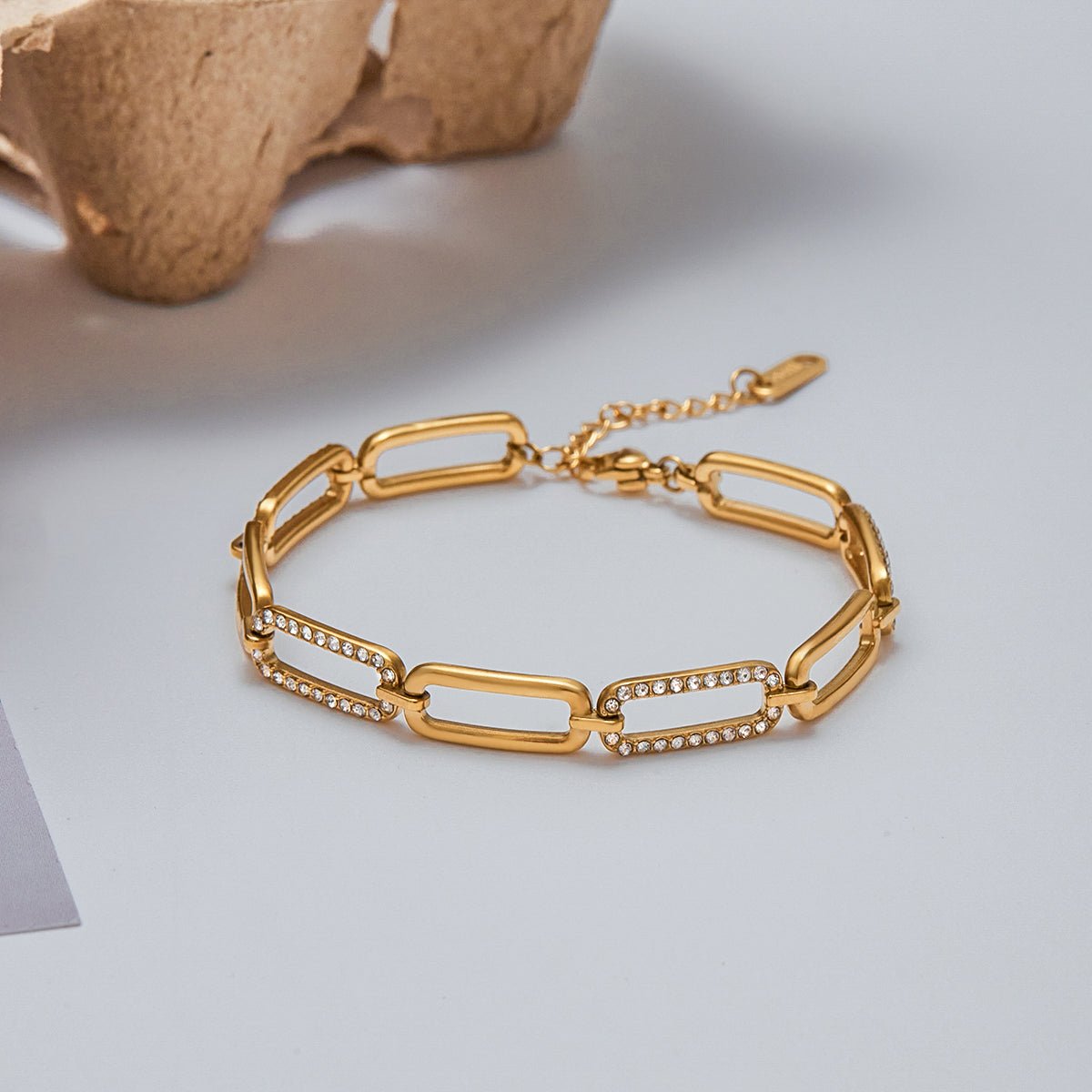 Gold chain bracelet with diamond accents on a light gray surface