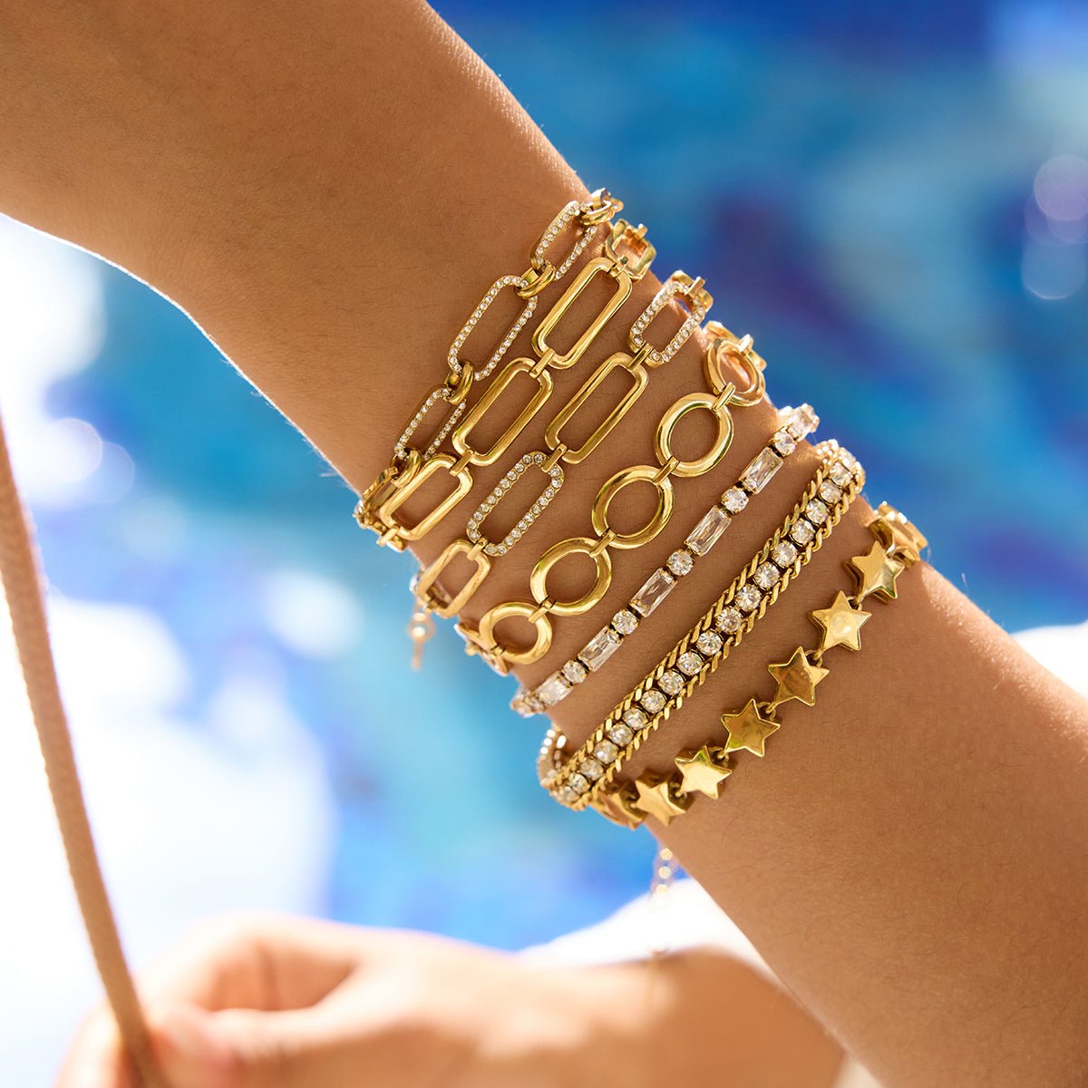 Multiple gold bracelets on a wrist with a blurred blue background