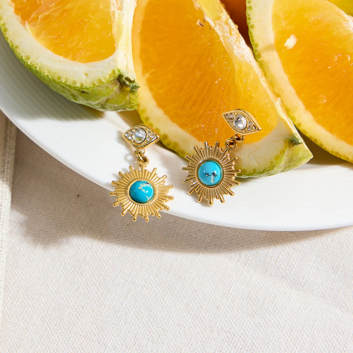 Gold earrings with turquoise stones on a plate of sliced pineapples.