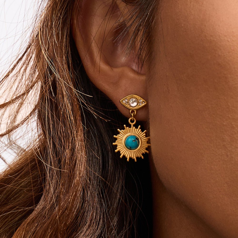 Gold earring with turquoise stone worn by a person with brown hair.