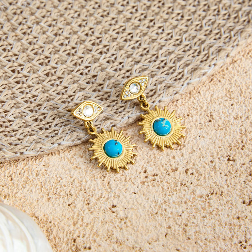 Gold earrings with turquoise stones on a textured beige surface