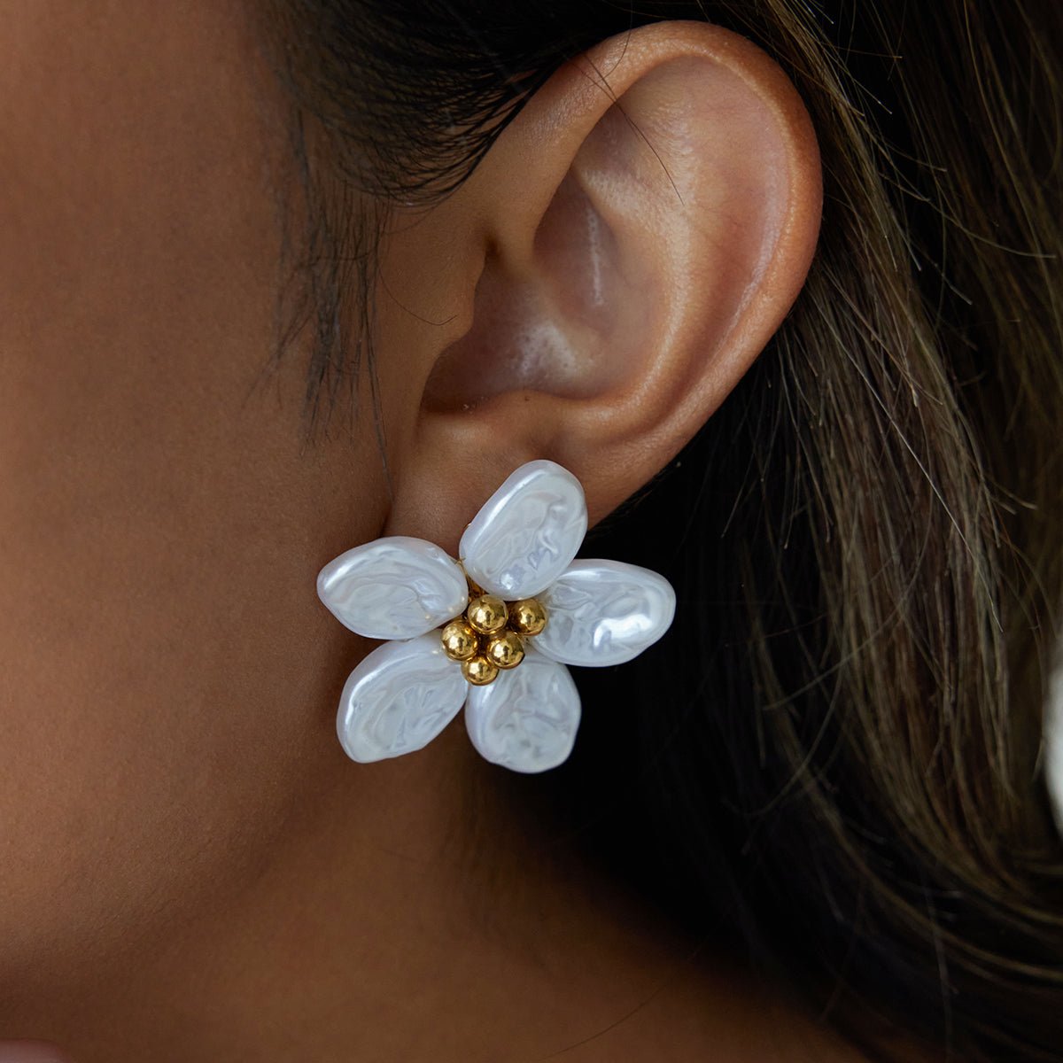 Close-up of a woman's ear wearing a white flower-shaped earring with gold center.