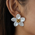 Close-up of a white floral earring with gold centers on an ear.