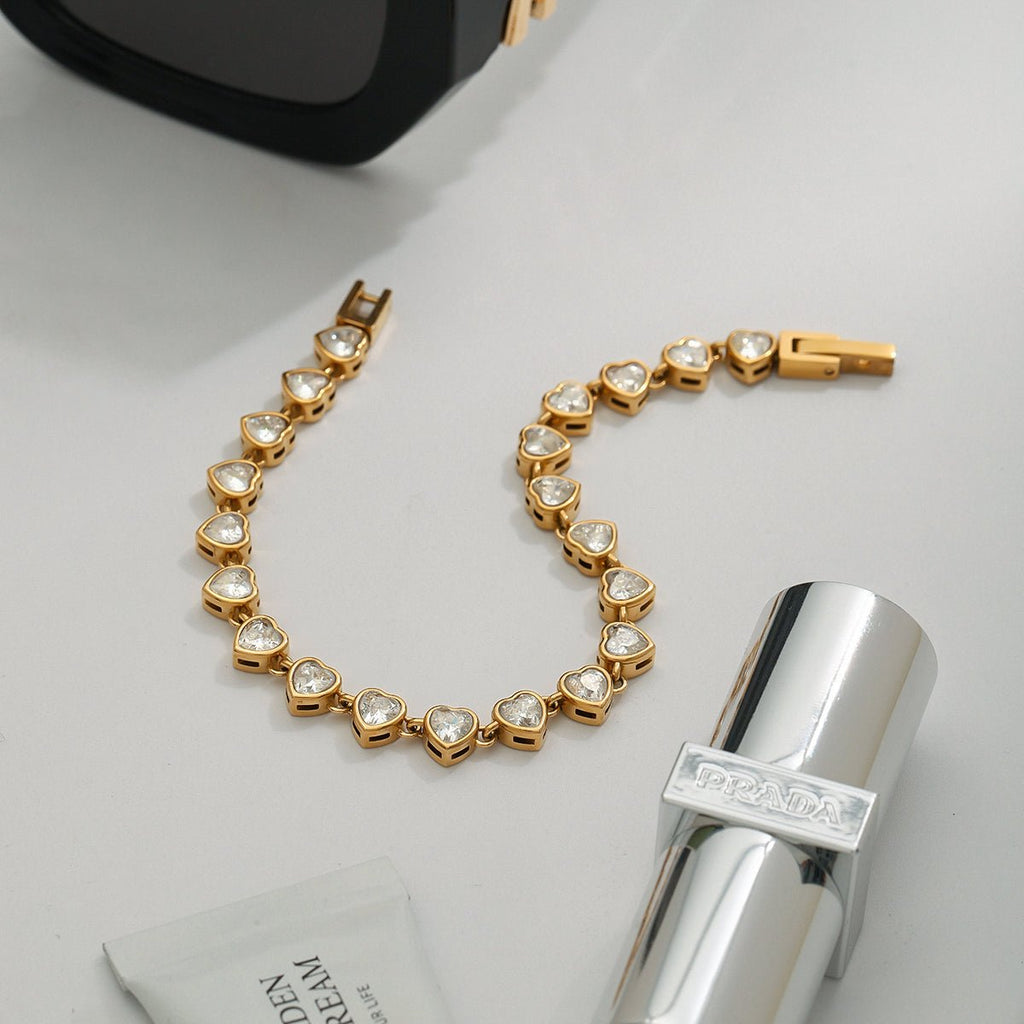 Gold bracelet with heart-shaped stones on a light gray surface with a silver bottle and black object.