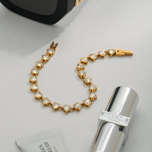 Gold bracelet with heart-shaped stones on a light gray surface with a silver bottle and black object.