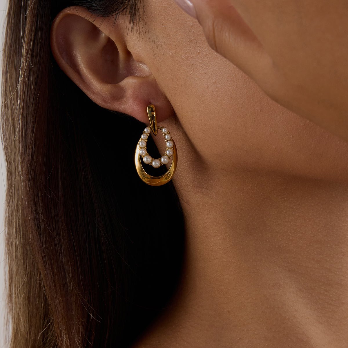 Gold hoop earring with black center and clear stones worn by a person.