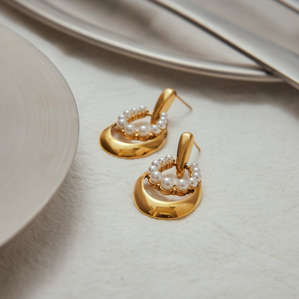 Gold heart-shaped earrings with pearls on a light surface