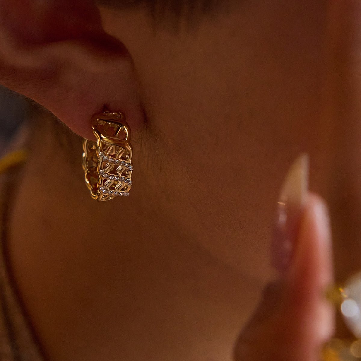 Close-up of a person wearing gold hoop earrings with small diamonds.