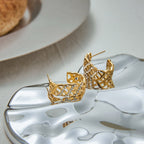 Gold earrings on a reflective surface with a blurred background