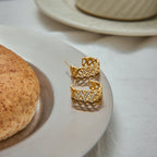 Gold earrings on a white plate with a light background