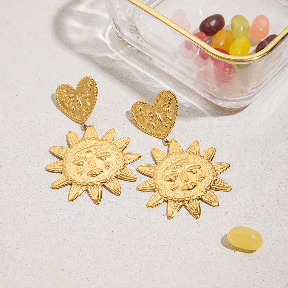 Gold sun-shaped earrings with heart tops on a light surface.