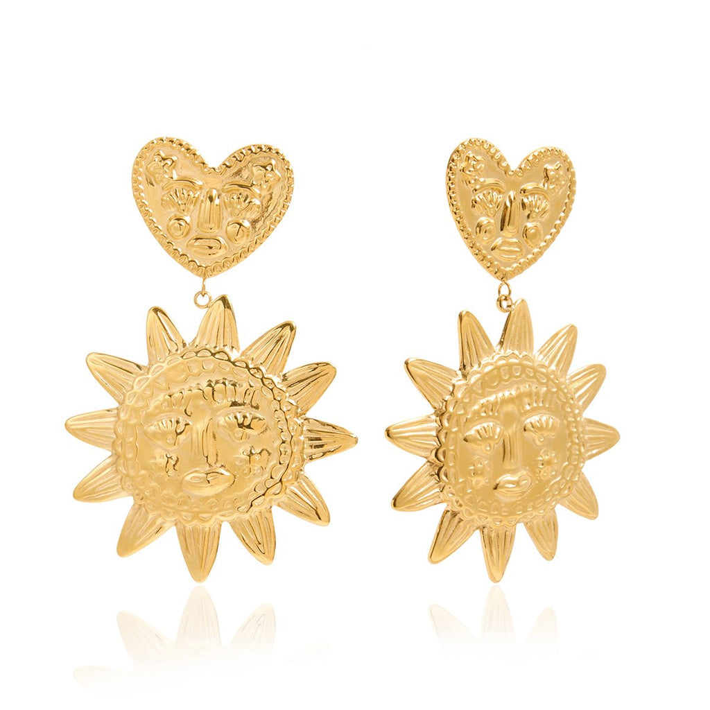 Pair of gold earrings with sun and heart designs on a white background