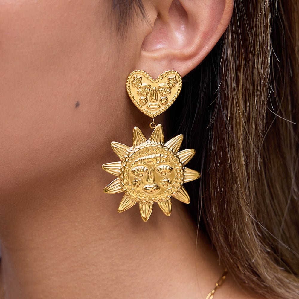 Gold heart and sun-shaped earrings worn by a person with brown hair.