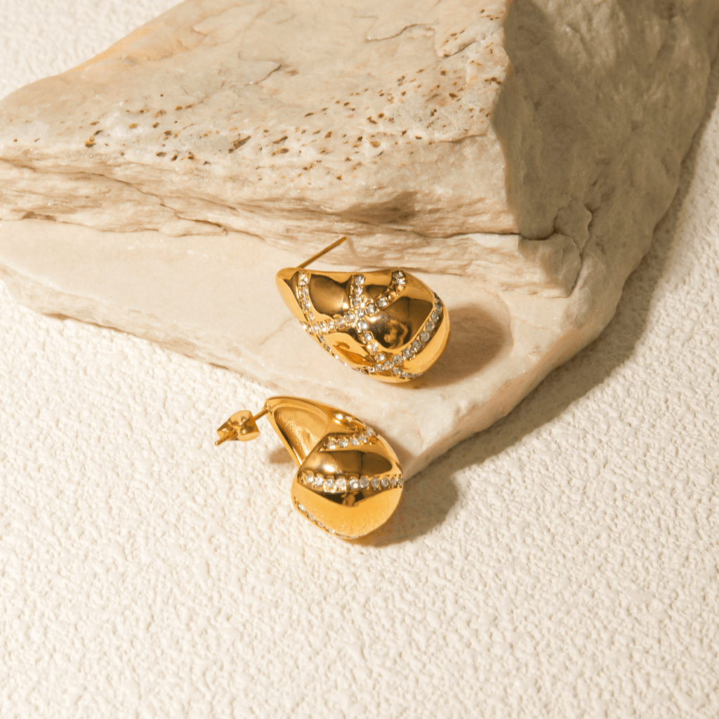 Gold earrings with diamond accents on a textured beige surface