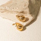 Gold earrings with diamond accents on a textured beige surface