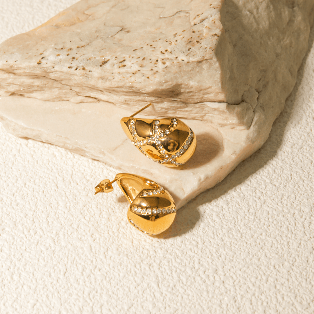 Gold earrings with diamond accents on a textured beige surface