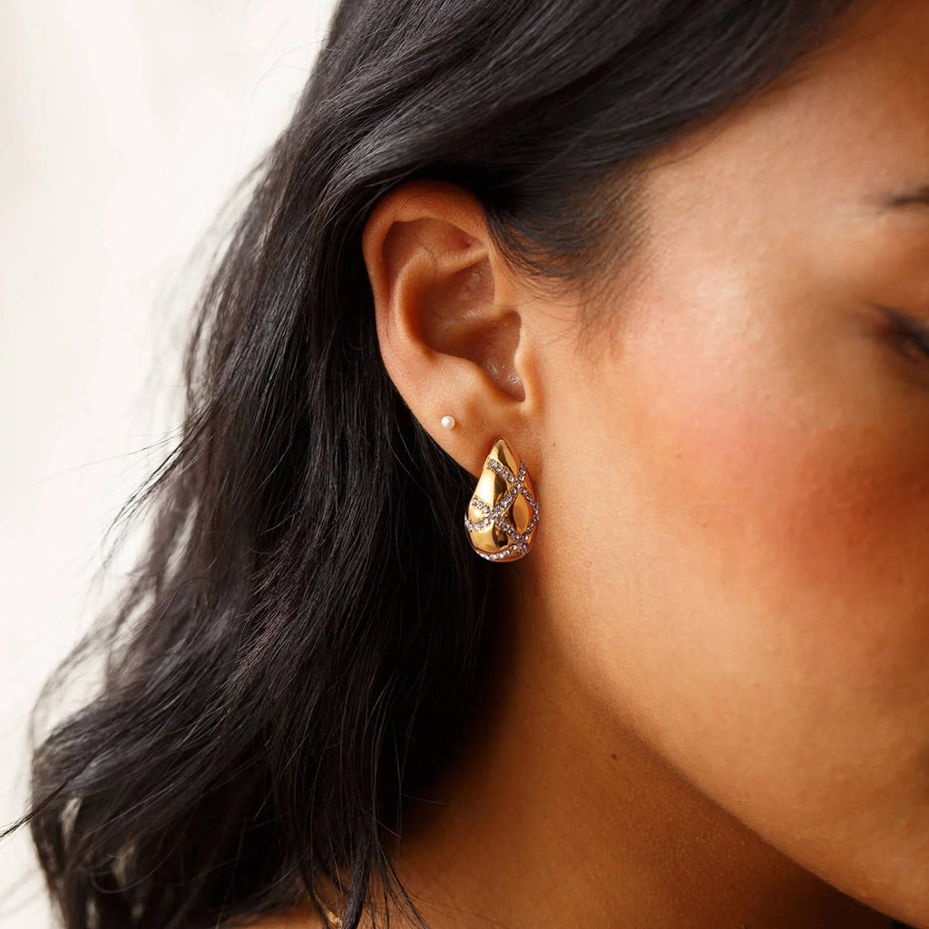 Close-up of a person wearing a gold teardrop earring with a blurred background