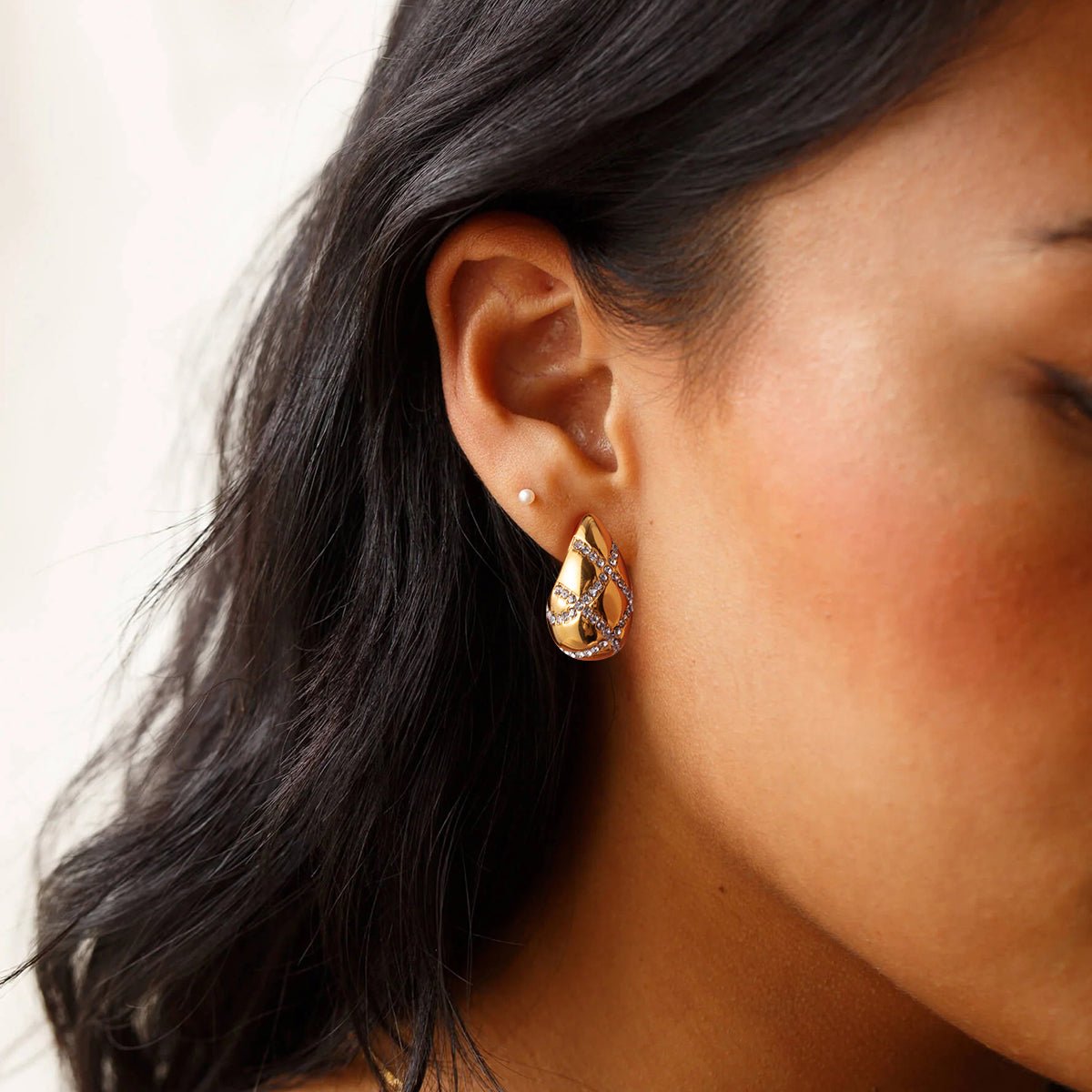 Close-up of a person wearing a gold teardrop earring with a blurred background
