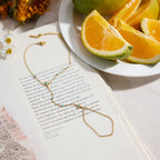Gold bracelet hand chain on an open book with orange slices and flowers in the background