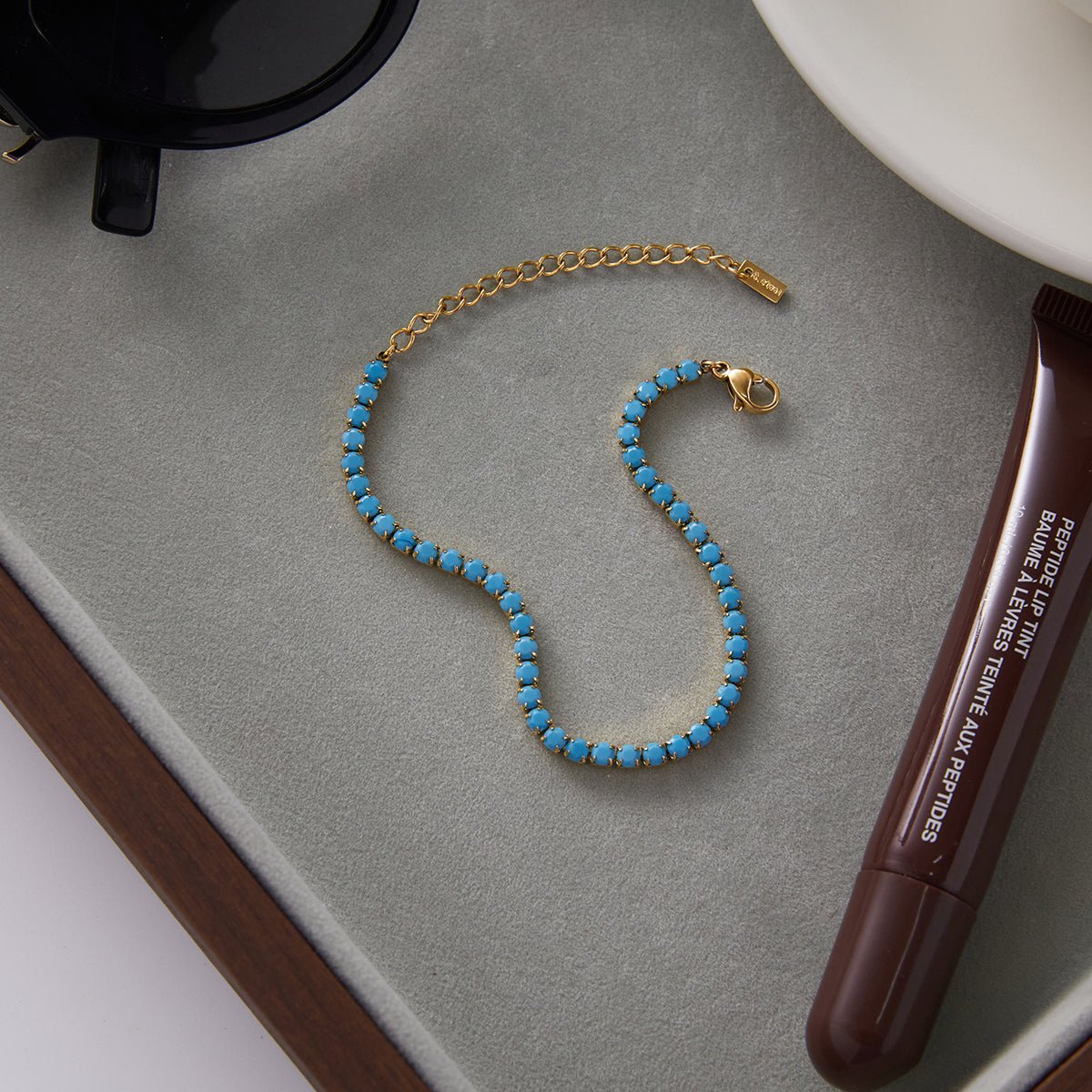 Blue beaded bracelet on a gray surface with a pen and sunglasses.