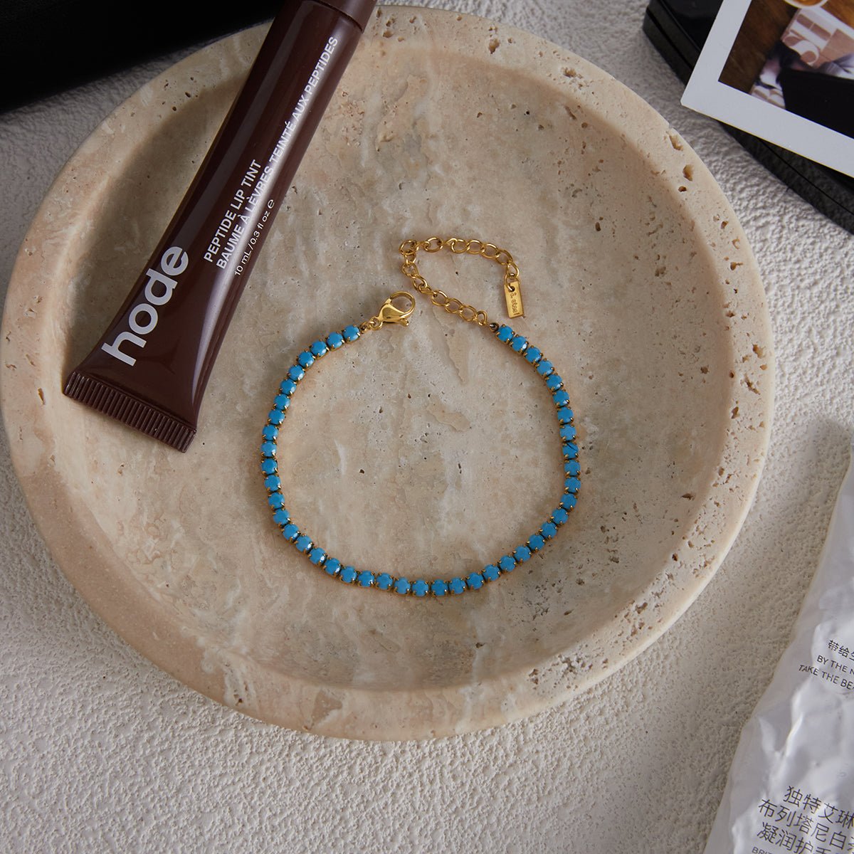 Blue beaded necklace on a beige plate with a brown tube of lip balm.
