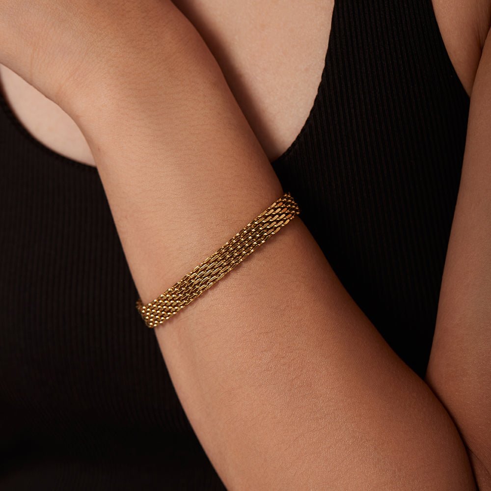 Gold bracelet on a person's wrist against a black background