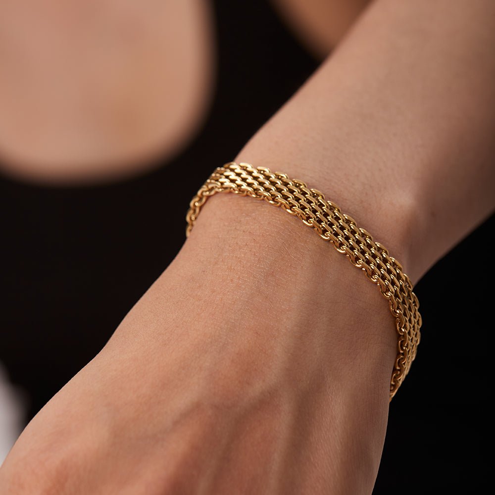 Gold chain bracelet on a wrist against a neutral background