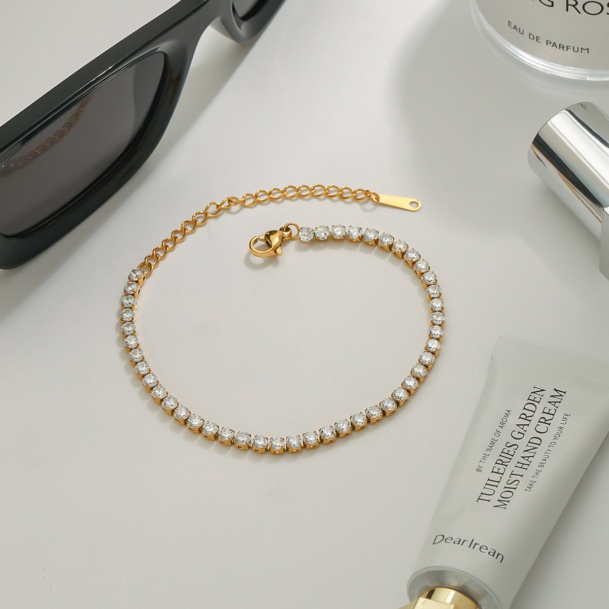 Gold bracelet on a surface with sunglasses and a skincare product.