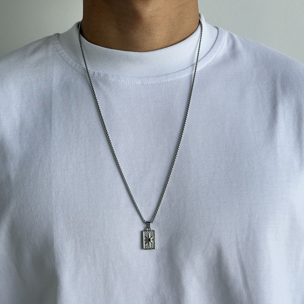 Person wearing a white shirt with a necklace featuring a rectangular pendant.