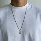 Person wearing a white shirt with a necklace featuring a rectangular pendant.
