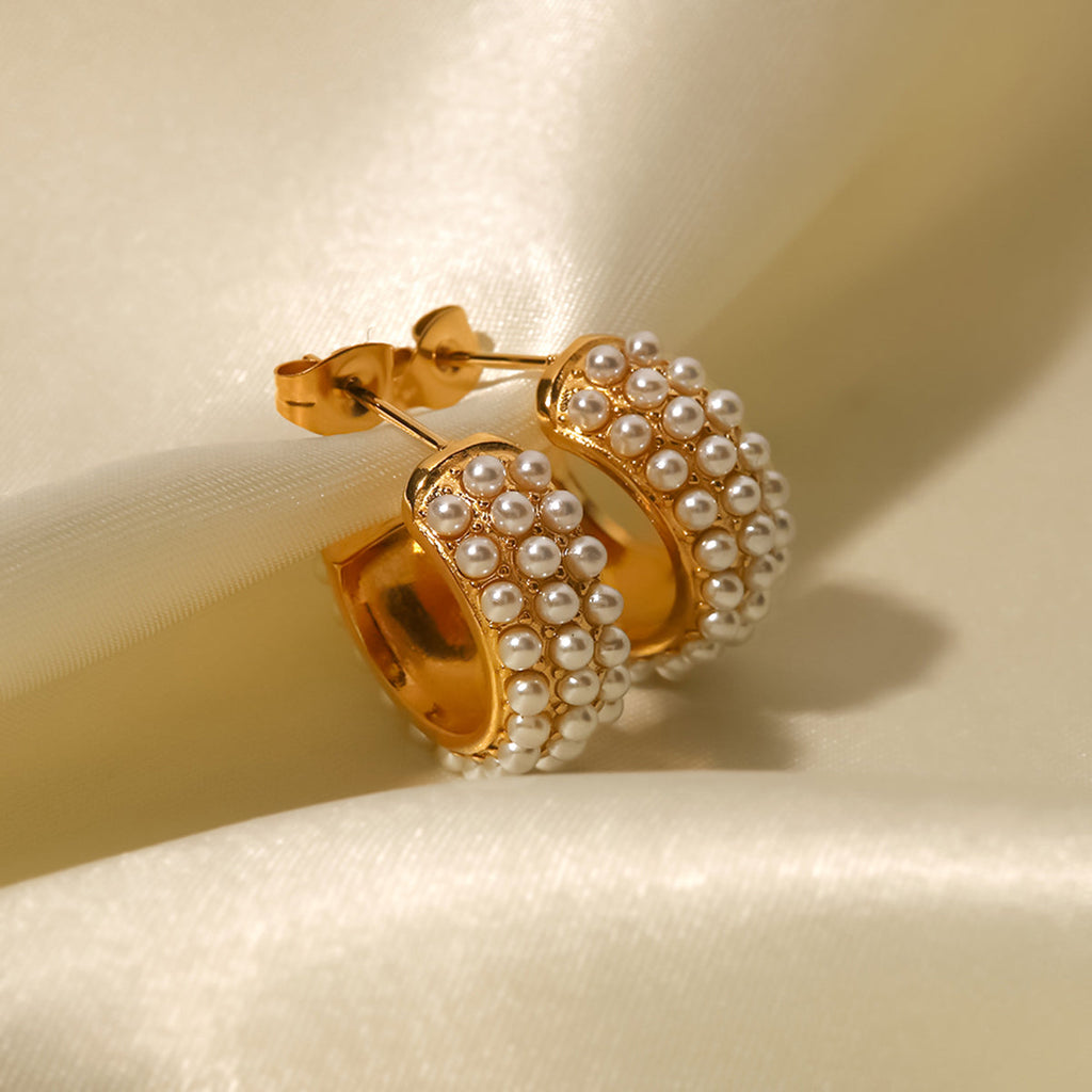 Gold hoop earrings with pearl accents on a beige background