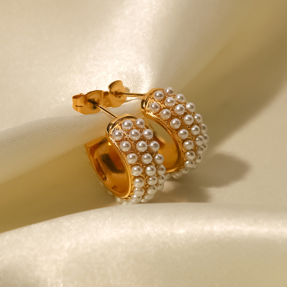 Gold hoop earrings with pearl accents on a beige background