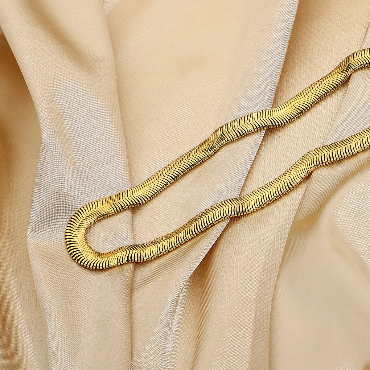 Gold snake-shaped necklace on beige fabric